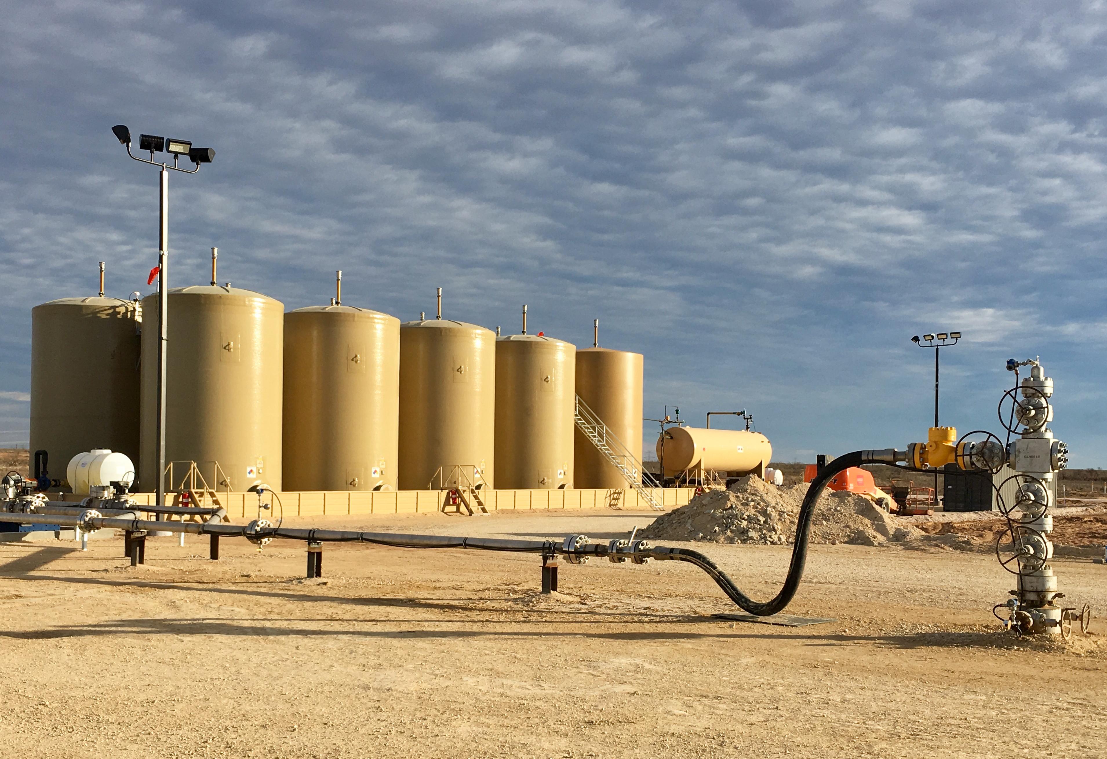 Oilfield water storage tanks, piping, and wellhead equipment under a cloudy sky